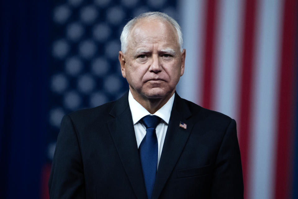 I don't know who this person is. The man in a suit stands in front of an American flag backdrop