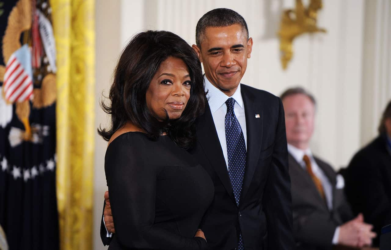 A man in a dark suit places his hand against the back of a woman in a black dress