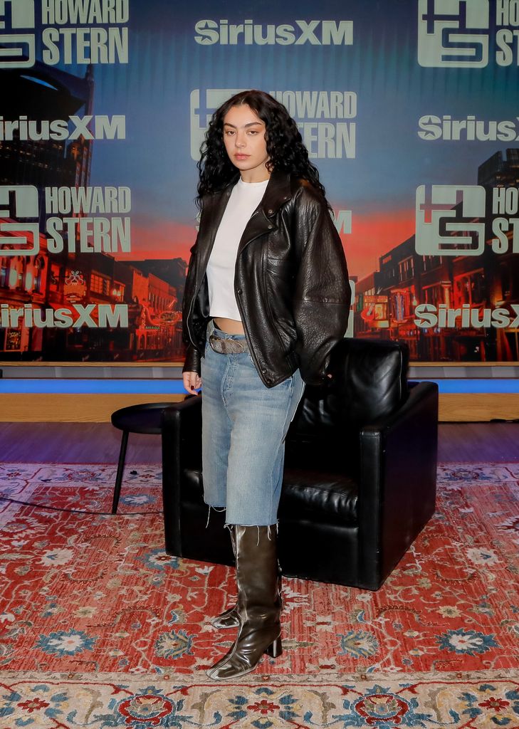 charli XCX poses in denim long shorts and bomber jacket