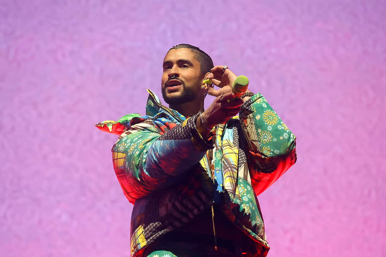 A man performs against a bright pink background in a multi-coloured puffer jacket