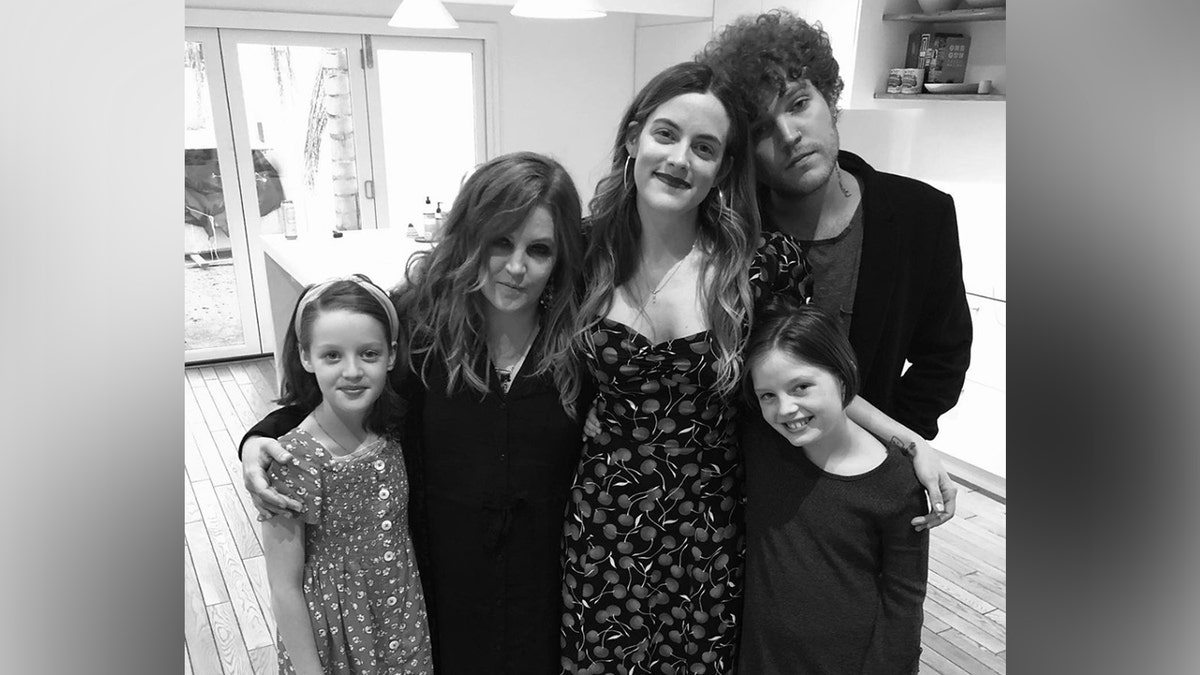 A black and white photo of Lisa Marie Presley hugging her four children, twins Harper Vivienne Ann Lockwood and Finley Aaron Love Lockwood on opposing ends, and daughter Riley Keough and son Benjamin Keough