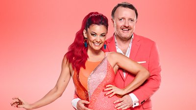 Dianne Buswell and Chris McCausland pose with Chris holding Dianne's waist. They both wear reddish orange outfits.