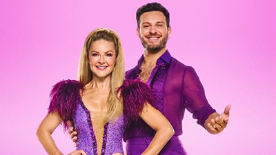 Sarah and Vito stand smiling wearing purple outfits