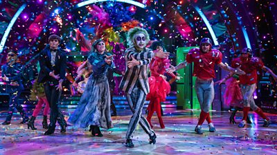 Strictly pro dancer Carlos Gu wears a black and white striped suit, white face paint and green wig as he leads the pro dancers in a Halloween routine